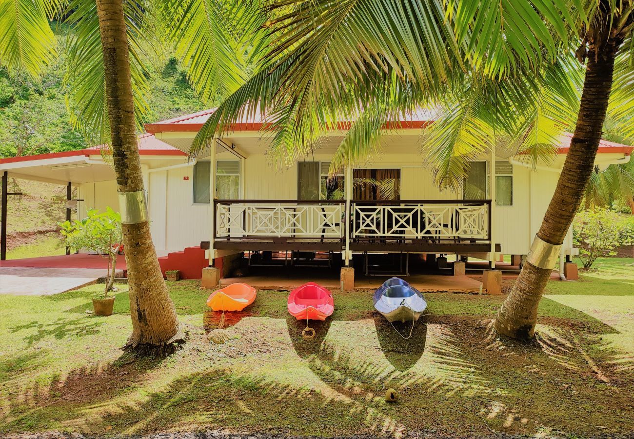 Ferienhaus in Huahine auf der Strandseite, mit Kajaks und Garten mit Bäumen.